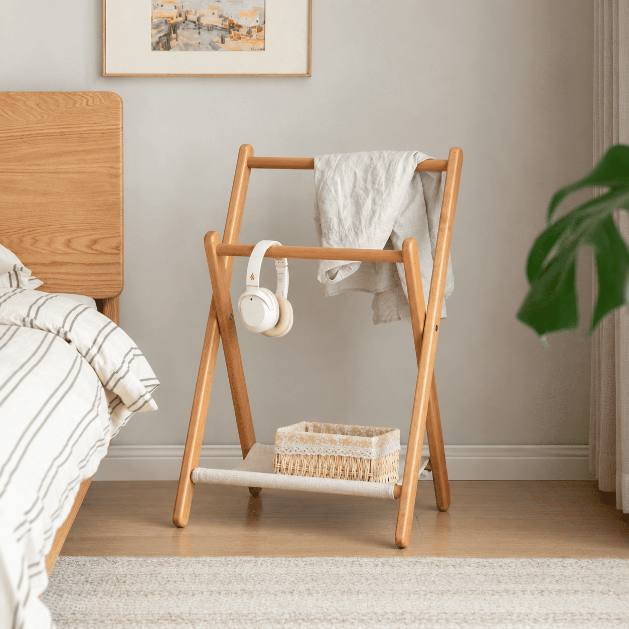 Naila natural solid beech folding coat rack styled beside bed in warm bedroom setting