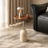 Round walnut side table with a travertine base and slim metal stem beside a black leather sofa