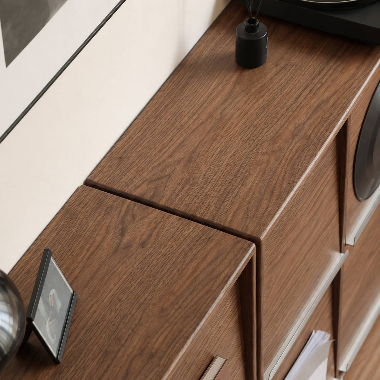 Close-up of walnut media cabinet with brushed metal display rail and integrated magazine storage slot.